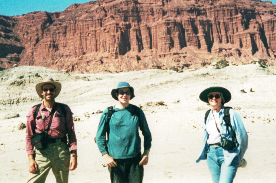 Three volunteers pose in front of red cliffs