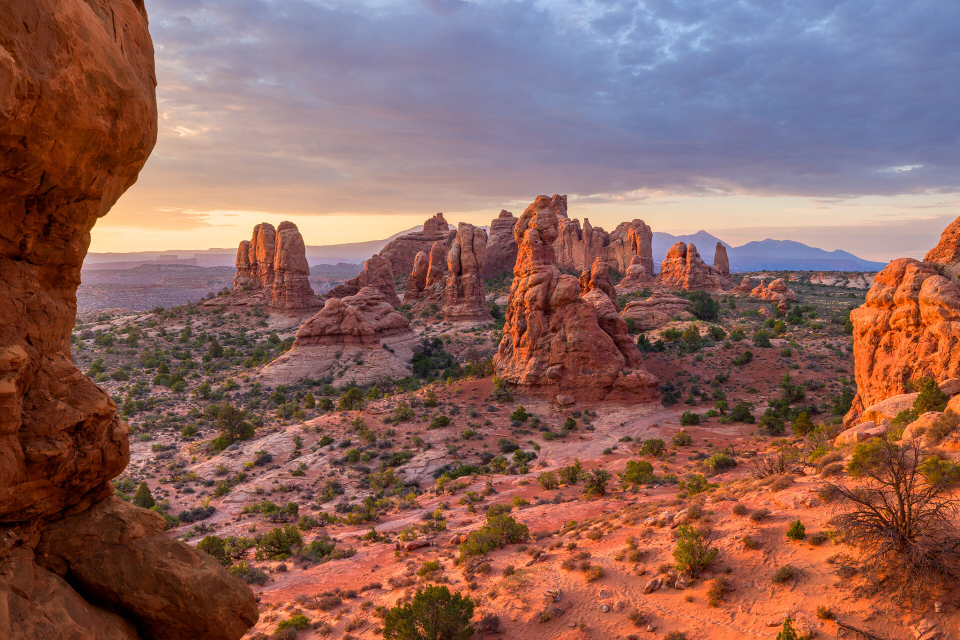 Towers in Arches National Park lit by the sunrise with clouds overhead.